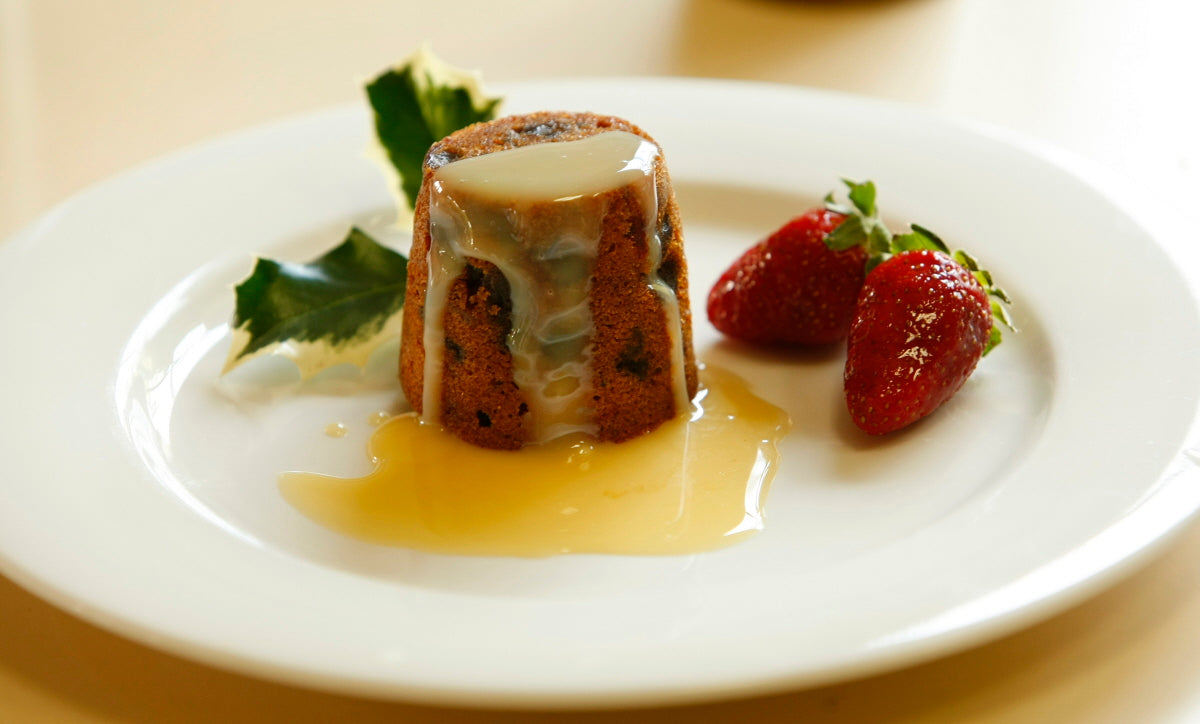 Traditional Christmas Plum Pudding 125 g served on a plate with custard – festive single-serve dessert, rich with fruits, brandy and spices.